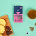 HotTea Mama - Organic The Final Push Raspberry Leaf Tea 20g on a blue background next to some cut pineapple and dates on a wooden chopping board and a glass cup of tea