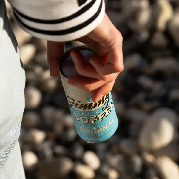 Hand holding a can of Jimmy's Iced Coffee Original SlimCan 250ml on the beach