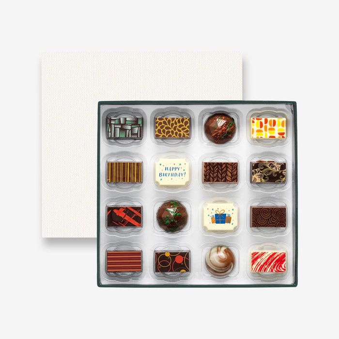 An open chocolate selection box containing 16 chocolates made by Harry Specters. The chocolates seen within this gift box are a colourful mix of white, milk, and dark chocolate with two Happy Birthday message chocolates.