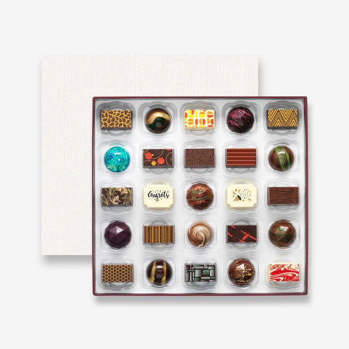 An open chocolate selection box containing 25 chocolates made by Harry Specters. The chocolates seen within this gift box are a colourful mix of white, milk, and dark chocolate with two Congratulations message chocolates.