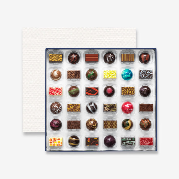 An open chocolate selection box containing 36 chocolates made by Harry Specters. The chocolates seen within this gift box are a colourful mix of white, milk, and dark chocolate.