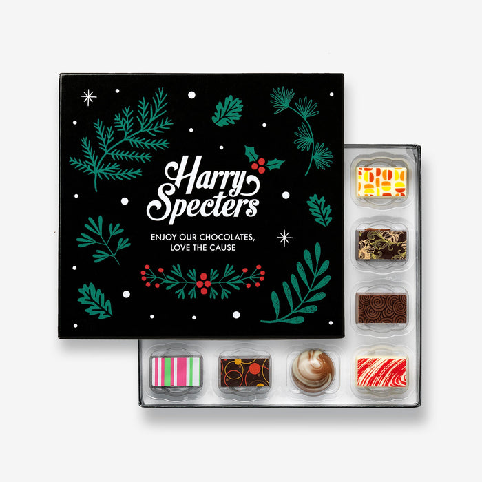 A Christmas chocolate selection box containing 16 chocolates, partially covered by a lid showing the name Harry Specters. The chocolates seen within this gift box are a colourful mix of white, milk, and dark chocolate with two Merry Christmas message chocolates.