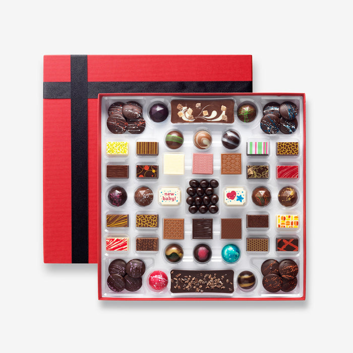 An open chocolate selection box containing 55 chocolates made by Harry Specters. The chocolates seen within this gift box are a colourful mix of white, milk, ruby, caramel, and dark chocolate with coffee beans, mini chocolate bars, and hot chocolate buttons with two New Baby themed chocolates.